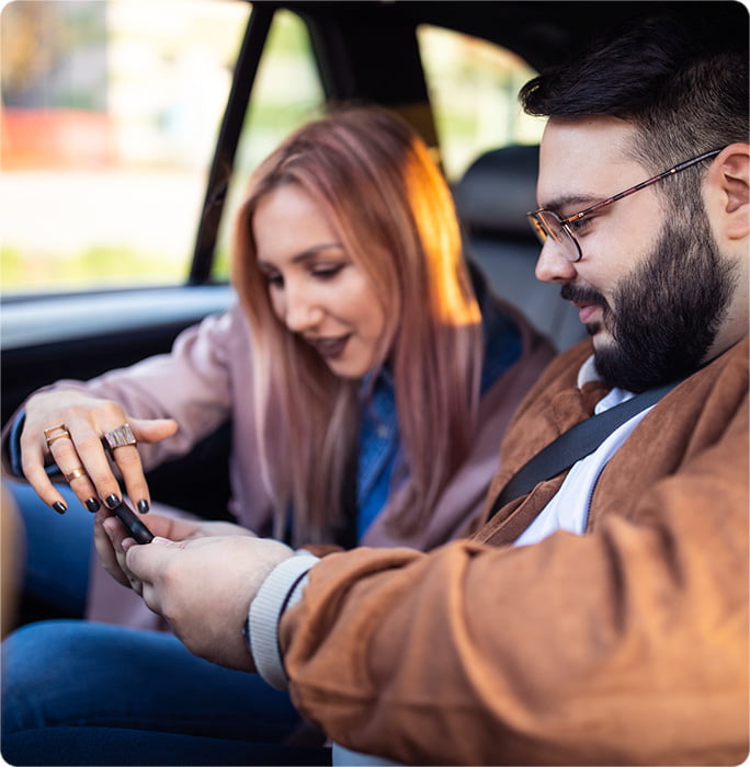Two individuals looking at a smartphone inside a car