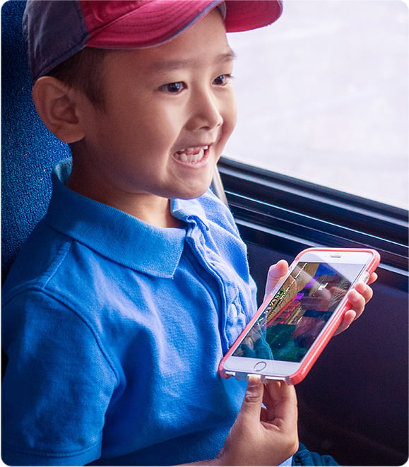 Young boy with baseball cap and blue polo smiles as he looks out of the window of an OC Bus.
