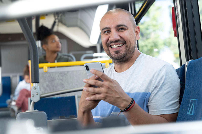 A male bus rider smiling while holding a phone