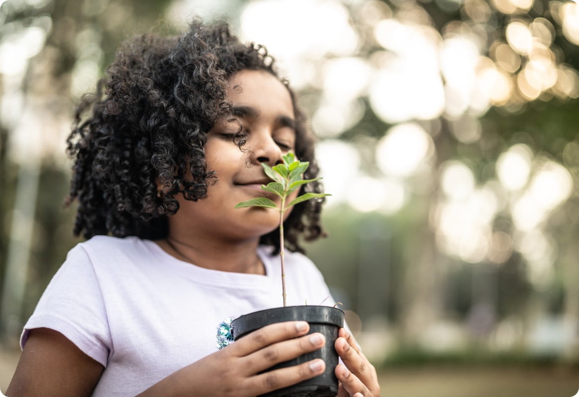 A young girl with closed eyes smells a plant happily