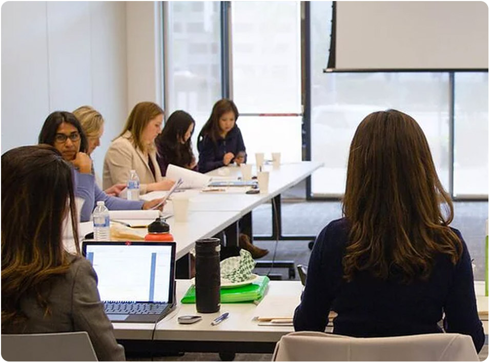 A large group of women sit with laptops in a round table format for discussion