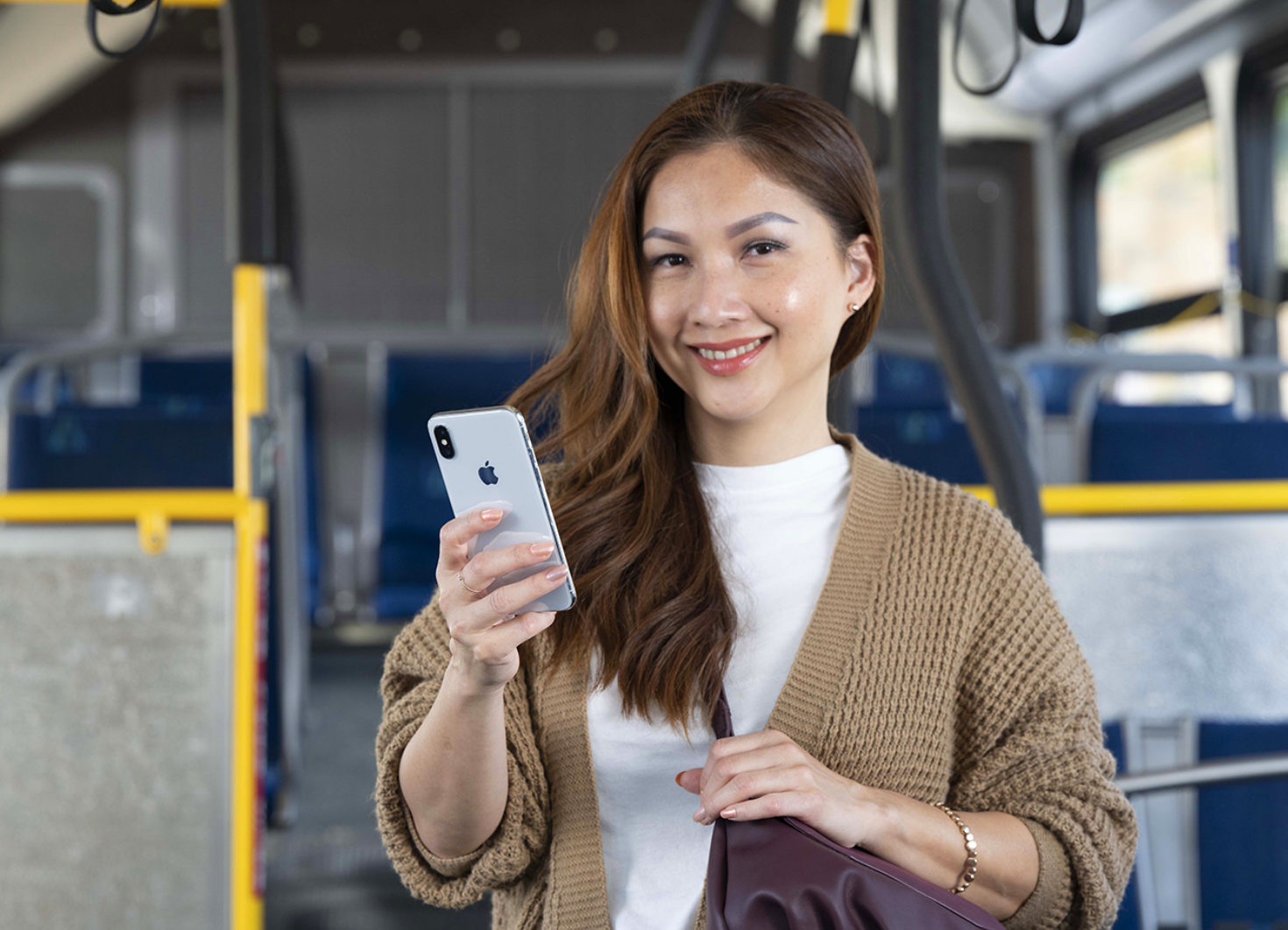 OC Bus rider standing on bus, smiling and holding smartphone