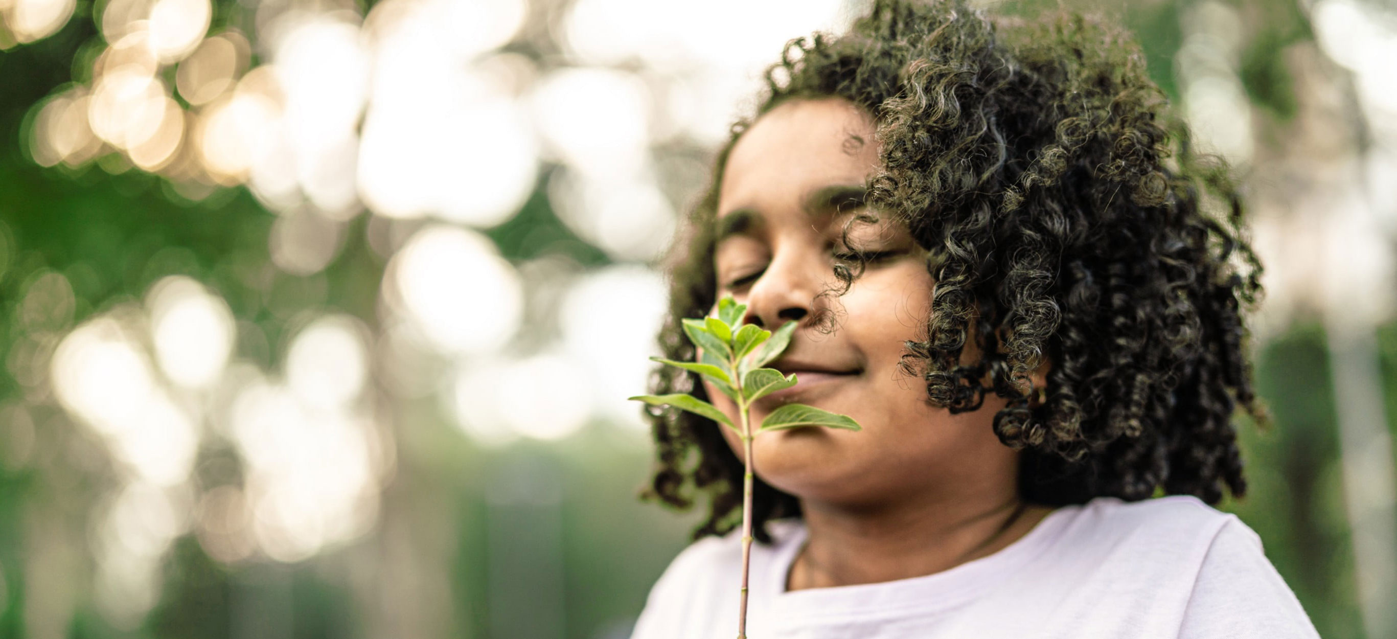 A young girl with closed eyes smells a plant happily