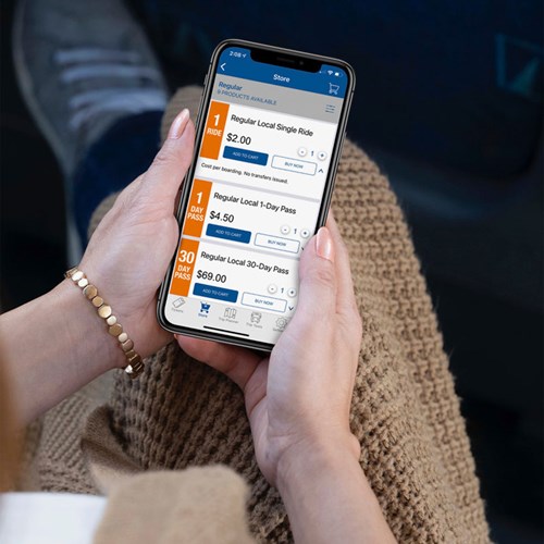 A woman's hands hold a phone showing the OC Bus App